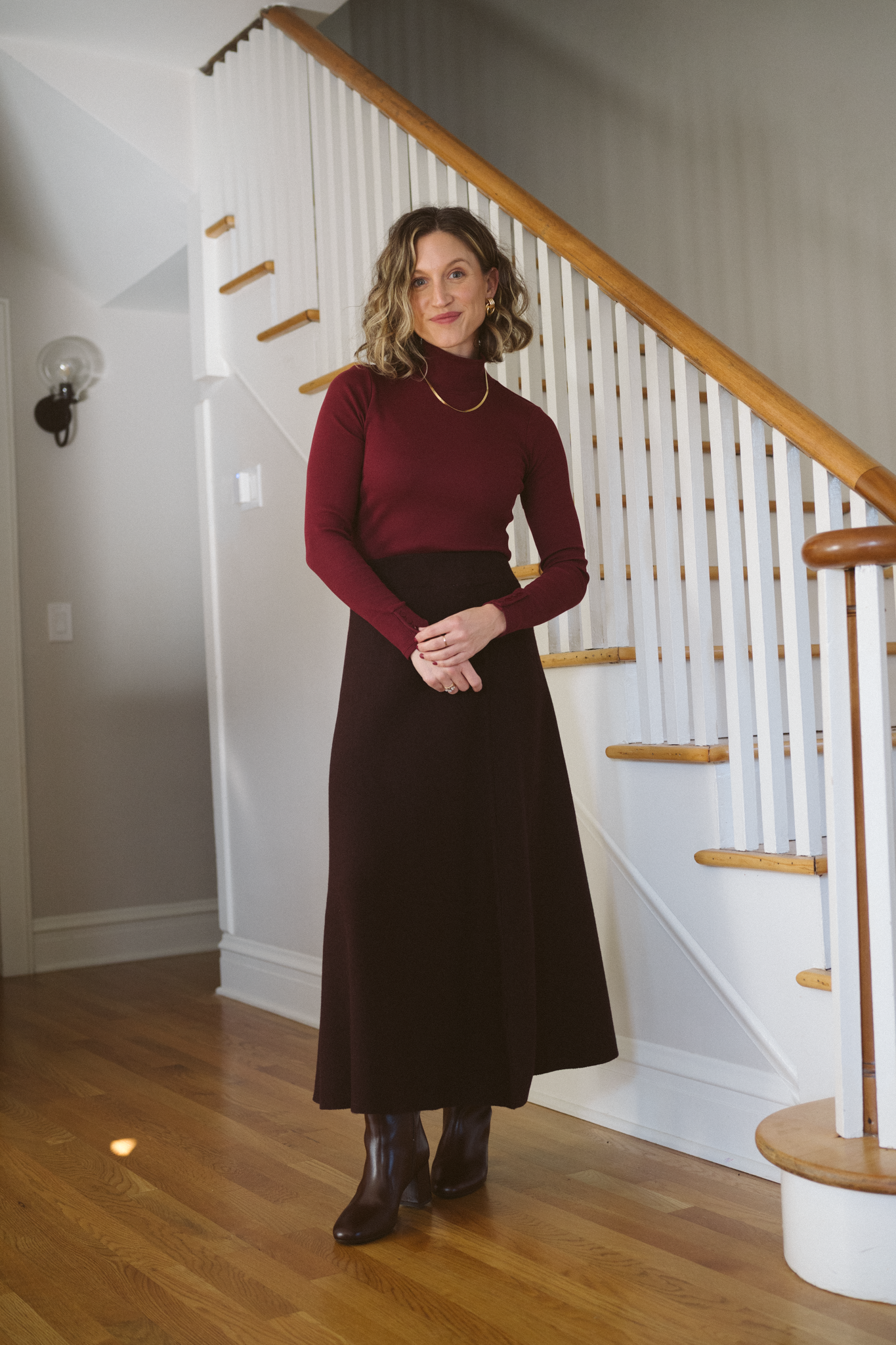 thanksgiving outfit with a burgundy mockneck sweater, brown knit midi skirt, and brown knee high boots